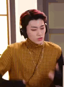 a young man wearing headphones and a yellow sweater is standing in front of a window .