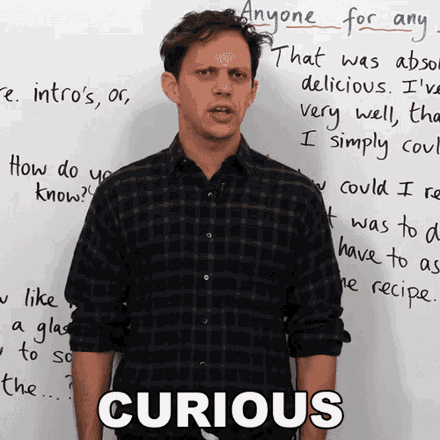 a man is standing in front of a white board with the word curious written on it
