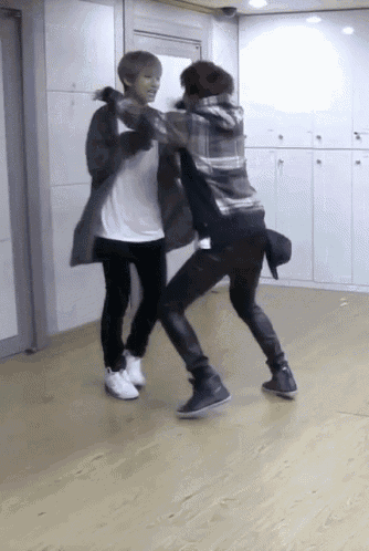 two young men are dancing on a wooden floor in a room
