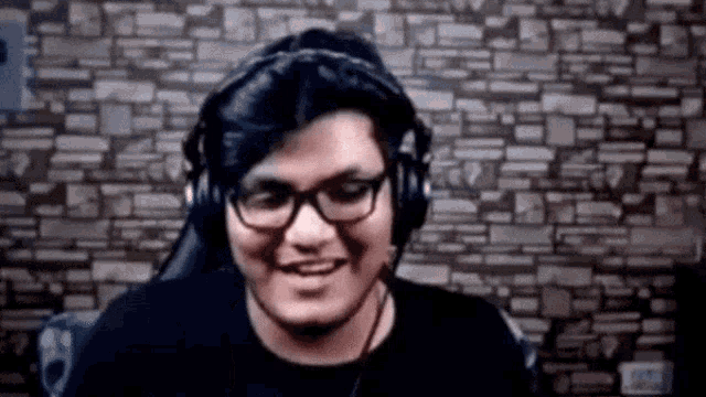 a man wearing headphones and glasses is smiling in front of a stone wall .