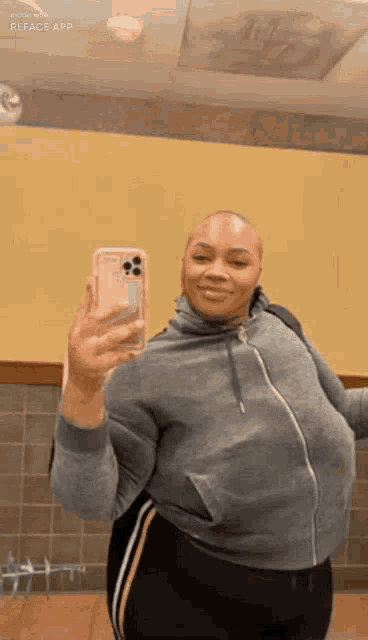 a woman is taking a selfie in front of a mirror with her phone .