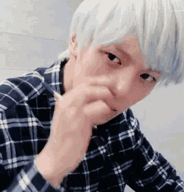 a young man with white hair is wearing a plaid shirt and covering his mouth .