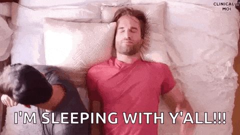 a man in a red shirt is sleeping on a bed with another man .