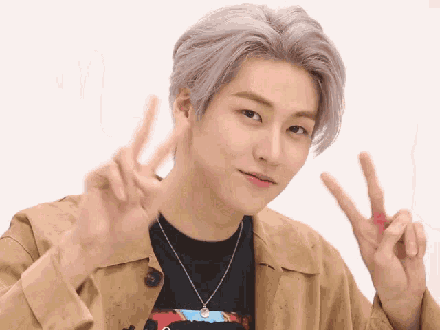 a young man wearing a tan jacket and a black shirt giving the peace sign
