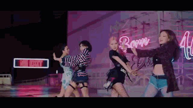 a group of women are dancing in front of a neon sign .