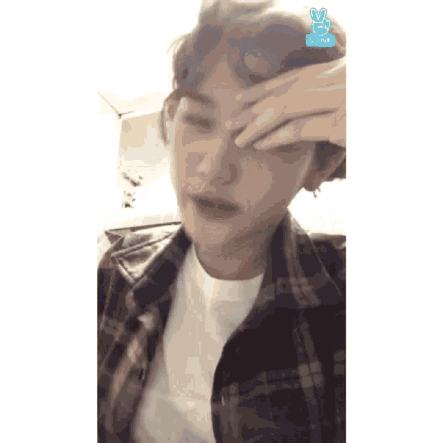 a man in a plaid shirt is covering his face with his hand and a blue sign that says vlive on it
