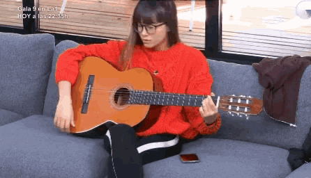 a woman in a red sweater is playing an acoustic guitar on a couch