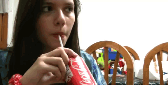 a girl is drinking a coca cola through a straw
