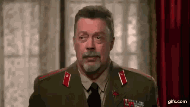 a man with a beard is wearing a military uniform and tie and looking at the camera .