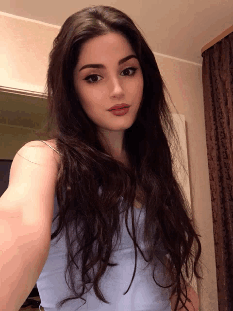 a woman with long dark hair takes a selfie in front of a brown curtain
