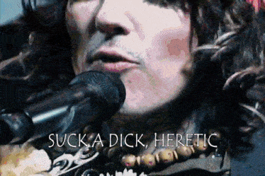 a man singing into a microphone with the words " suck a dick heretic " above him