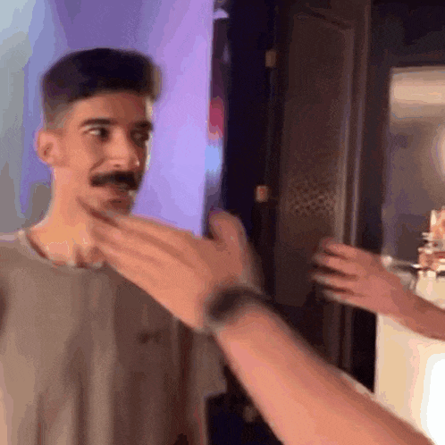 a man with a mustache is touching another man 's face .