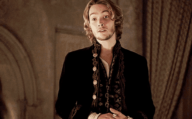 a man with long blonde hair and a beard is wearing a black jacket and vest with gold buttons