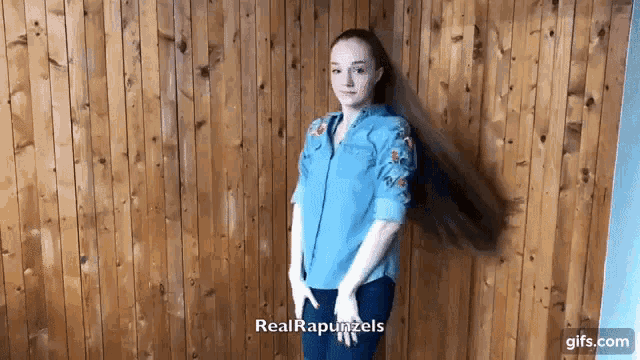 a young woman with long hair is standing in front of a wooden wall .