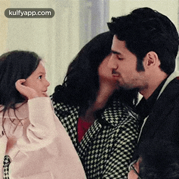 a man is kissing a woman on the cheek while a little girl looks on .