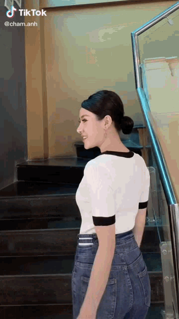 a woman in a white shirt and blue jeans is standing next to stairs .