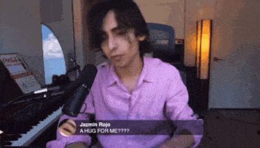 a man in a pink shirt is sitting in front of a microphone and asking for a hug