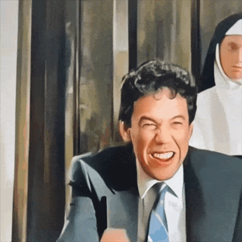 a man in a suit and tie is smiling with a nun in the background