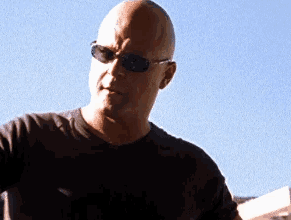 a man wearing sunglasses and a black shirt looks at the camera