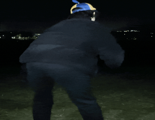a person wearing a black jacket and a blue hat is standing in the dark