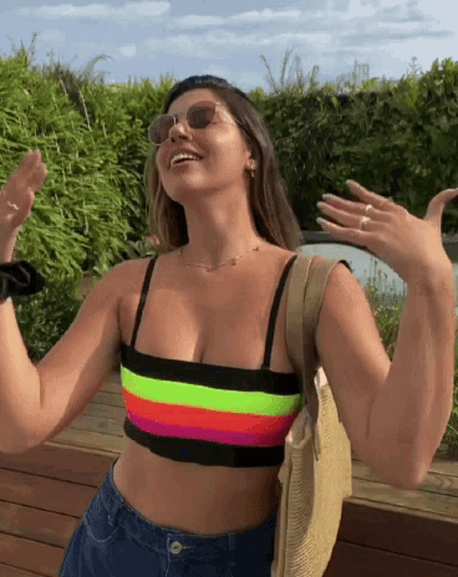 a woman wearing sunglasses and a colorful crop top is smiling