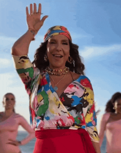 a woman in a colorful top and red skirt is waving