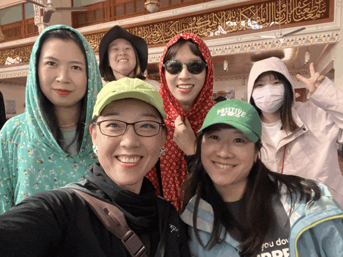 a group of women posing for a picture with one wearing a green positive hat