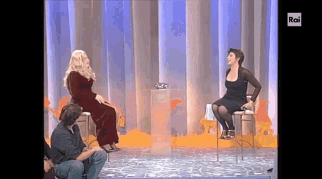 a woman in a wig sits next to a woman in a black dress on a television show that says rai on the screen