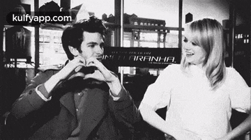 a black and white photo of a man and woman making a heart shape with their hands .