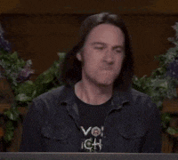 a man is sitting at a table with flowers in the background and making a funny face .
