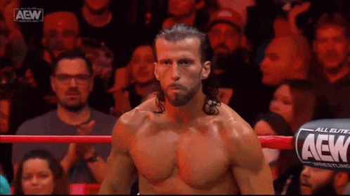 a wrestler without a shirt is standing in a ring with a crowd watching .
