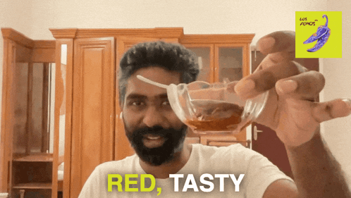 a man with a beard is holding a glass with a spoon in it and says red tasty