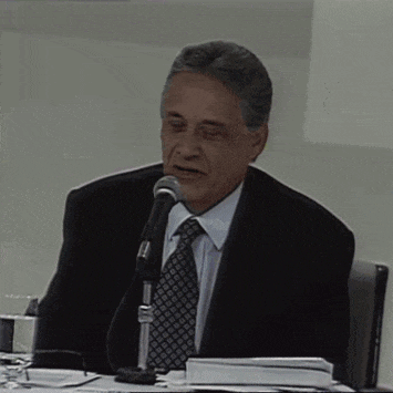 a man in a suit and tie is sitting at a table speaking into a microphone