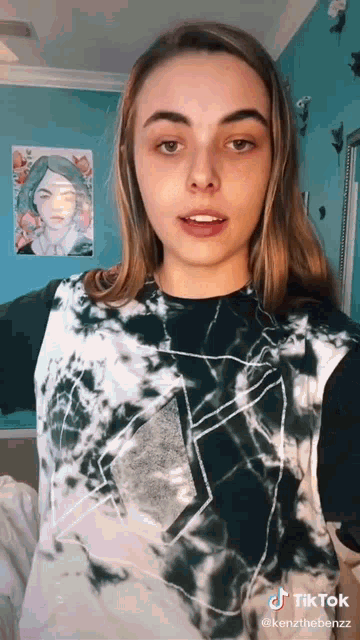a woman wearing a tie dye shirt is standing in front of a blue wall with a picture on it .