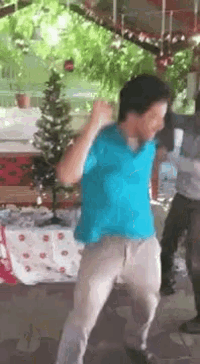 a man in a blue shirt and khaki pants is dancing in front of a christmas tree
