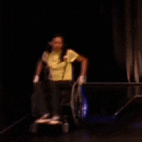 a woman in a yellow shirt is sitting in a wheelchair in the dark
