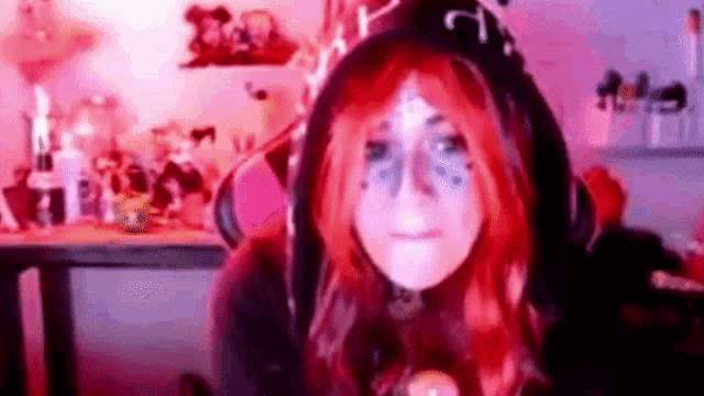 a woman with red hair is wearing a hoodie and headphones while sitting in a chair .