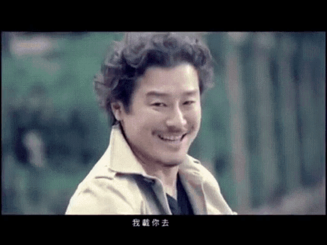 a man in a trench coat is smiling with chinese writing on the screen behind him