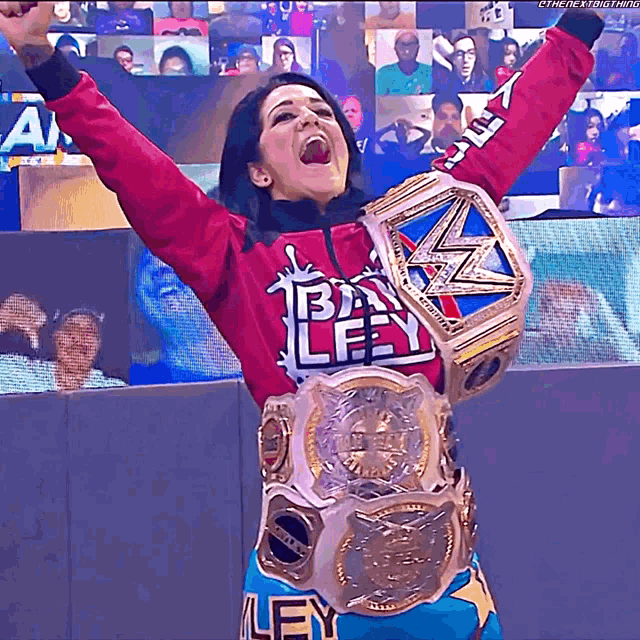 a woman wearing a shirt that says bayley is holding up her arms in the air