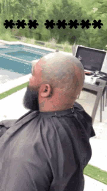 a bald man with a beard is sitting in front of a laptop