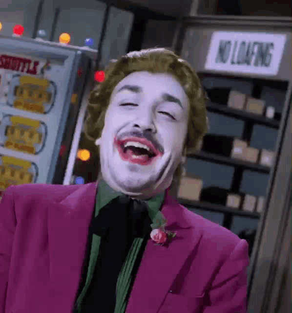 a man in a joker costume is laughing with his eyes closed in front of a no loafing sign .