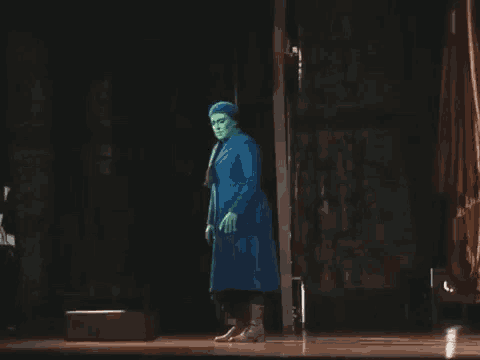 a man with green paint on his face is standing on a stage in a blue coat .