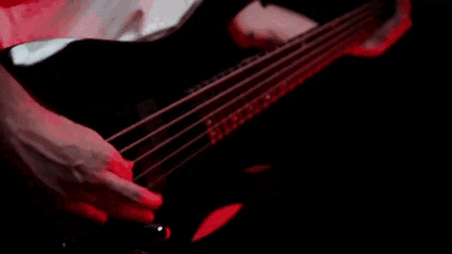 a man is playing a bass guitar in a dark room with red lights behind him