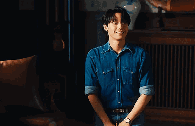 a man wearing a blue denim shirt is smiling in a dark room