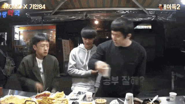 a group of young men are standing around a table with a sign above them that says momo x 1984