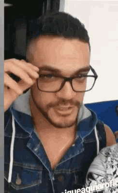 a man wearing glasses and a denim jacket has the word aguila on the bottom of his shirt