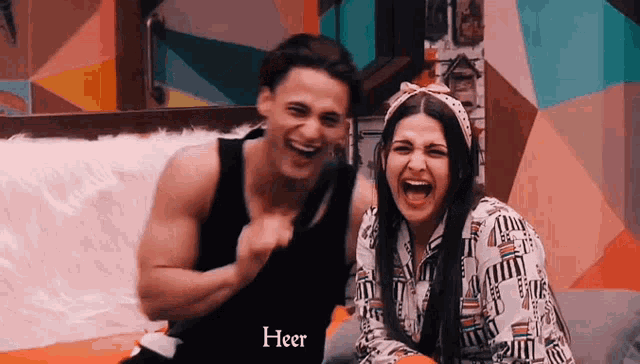a man and a woman are laughing with the word heer on the bottom right