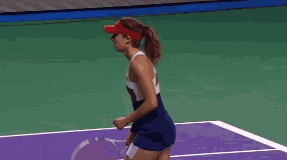 a woman wearing a red visor is kneeling on a tennis court