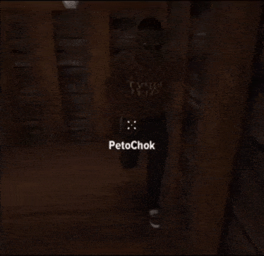 a man in a plaid shirt is standing in a dark room with the name petochok written on his shirt