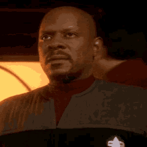 a bald man with a beard wearing a star trek uniform looks down at something